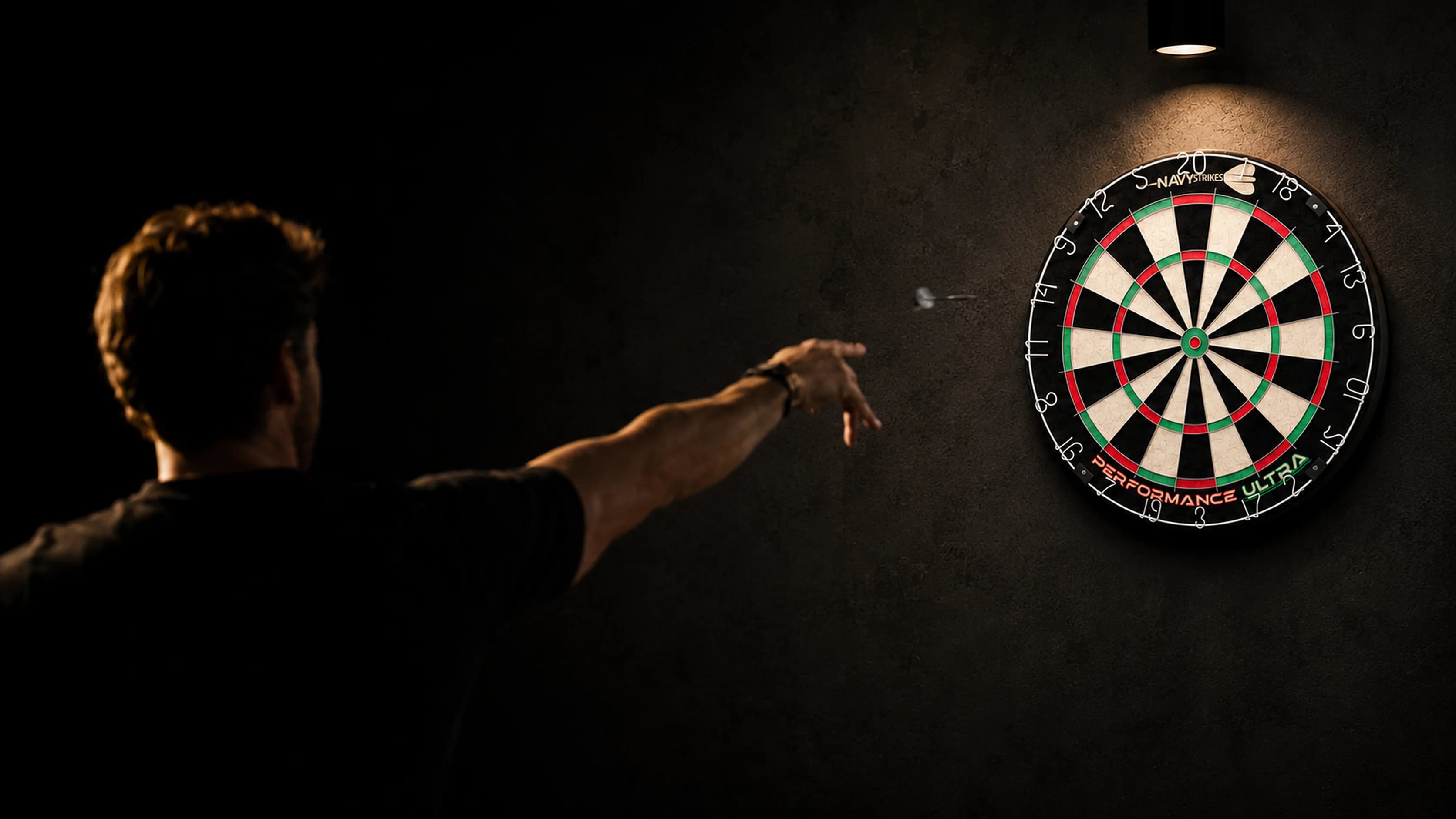 Darter gooit een pijl richting een Navy Strikes Performance Ultra dartbord in een sfeervol verlichte thuisruimte
